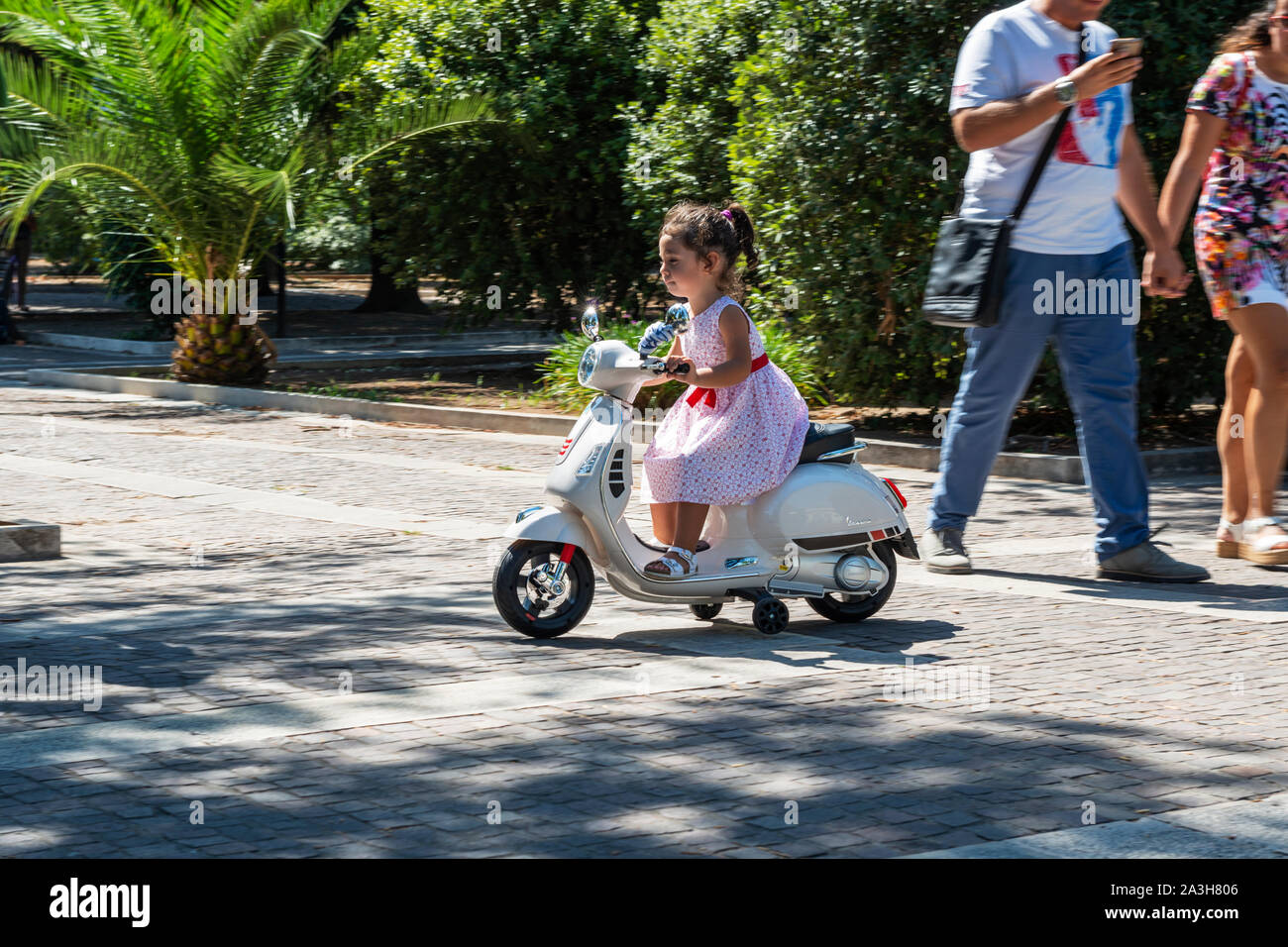 Young girl riding toy scooter in Villa Comunale public garden (Giardini Pubblici Giuseppe Garibaldi) in Lecce, Apulia (Puglia) in Southern Italy Stock Photo