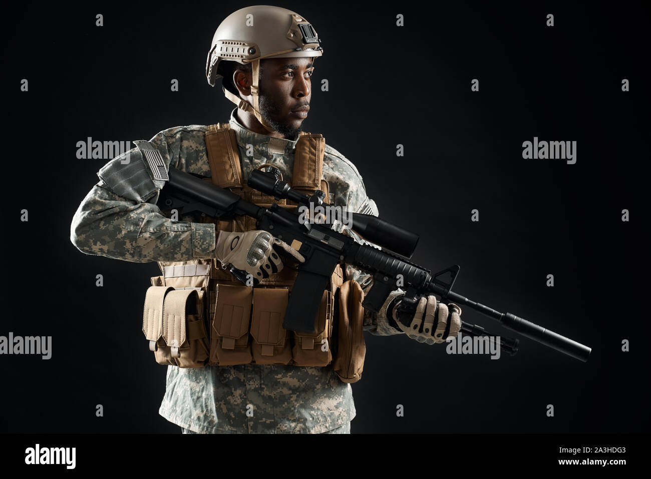 Confident young soldier wearing Americans army uniform and glasses holding weapon machine in hands and keeping position. African man preparing for war, protecting homeland. Stock Photo