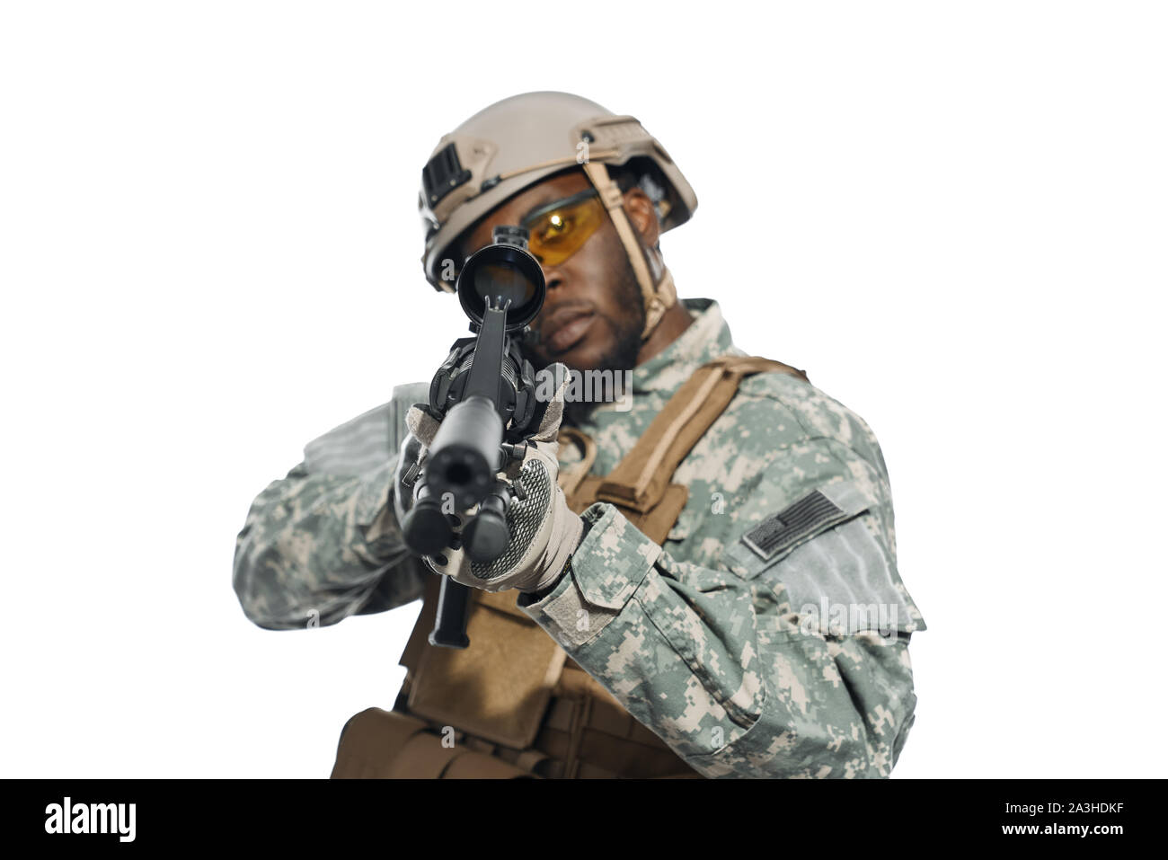 Front view of professional American soldier aiming with weapons machine in camera. African male serve in army, wearing helmet, armour and yellow glasses, keeping position. Concept of war. Stock Photo