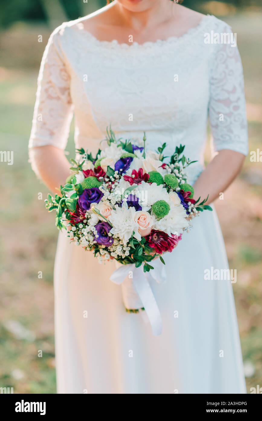 Hands of bride with wedding beautiful bouquet of white, purple and pink