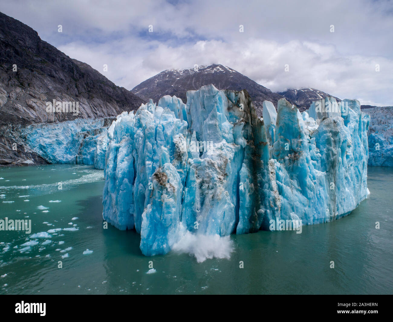 USA, Alaska, Tracy Arm - Fords Terror Wilderness, Aerial view of iceberg calving from blue face of Dawes Glacier on summer morning Stock Photo