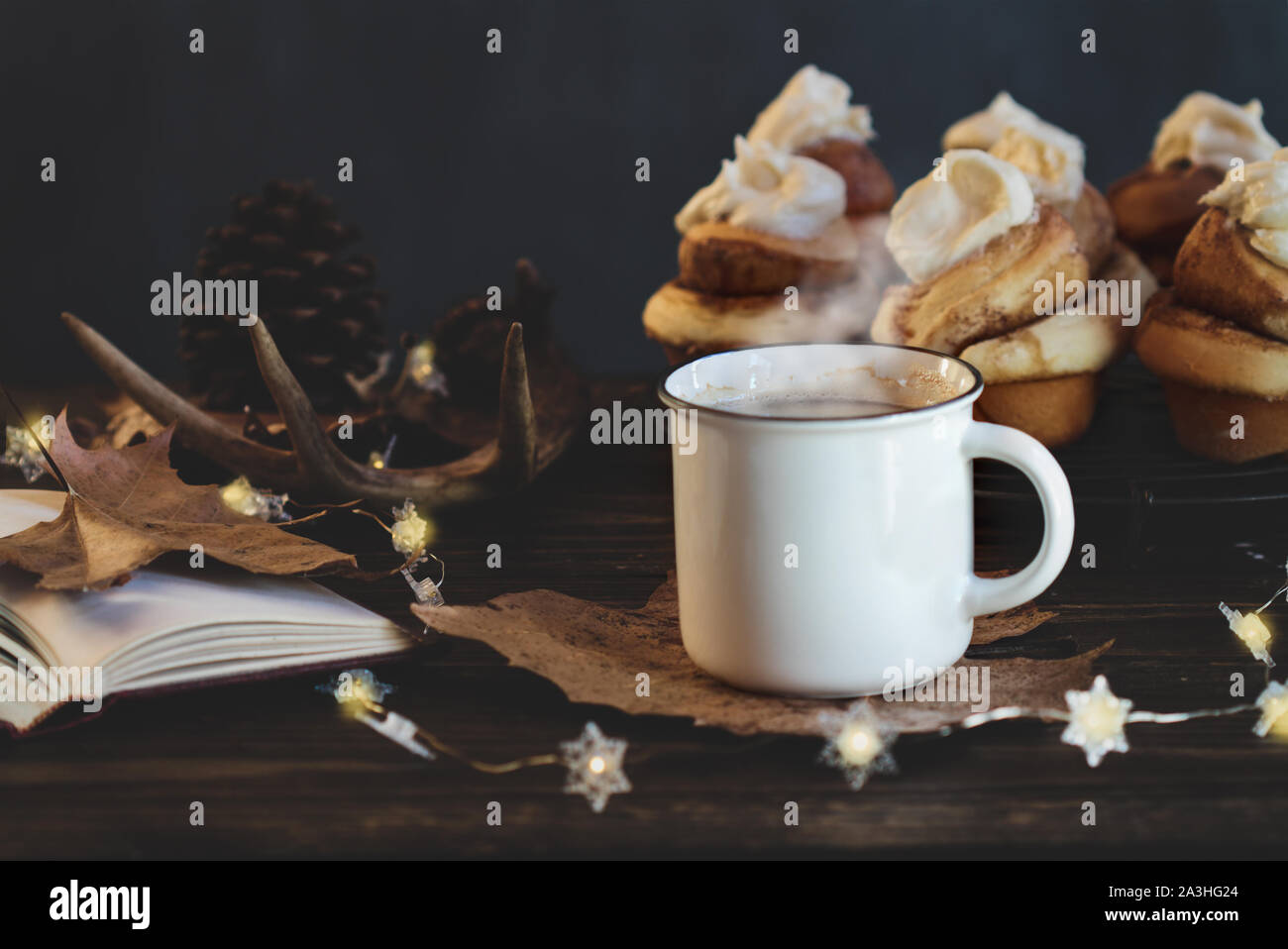 Hot, steaming cup of coffee with cinnamon rolls and open book Selective focus on drink with extreme blurred foreground and background. Stock Photo