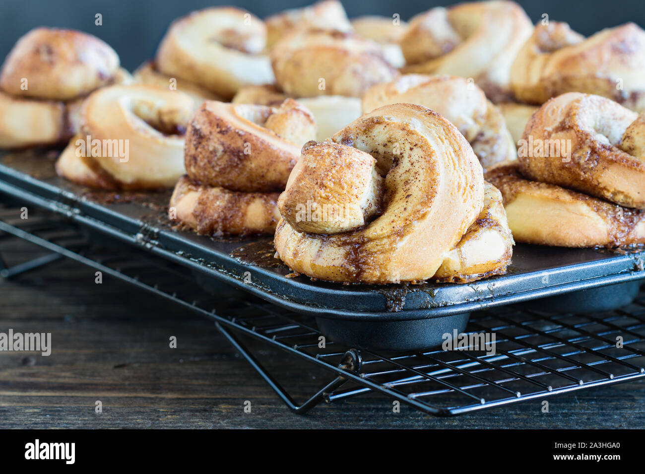 Fresh homemade tall cinnamon rolls still in the muffin tin over a rustic wood table. Selective focus on bun in the foreground with blurred background. Stock Photo