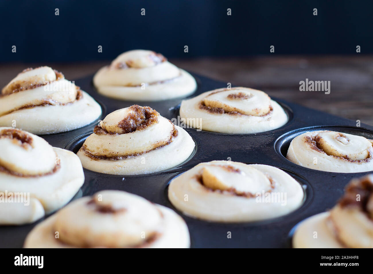 Homemade tall cinnamon roll rising in a muffin tin. Selective focus on center with blurred foreground and background. Stock Photo