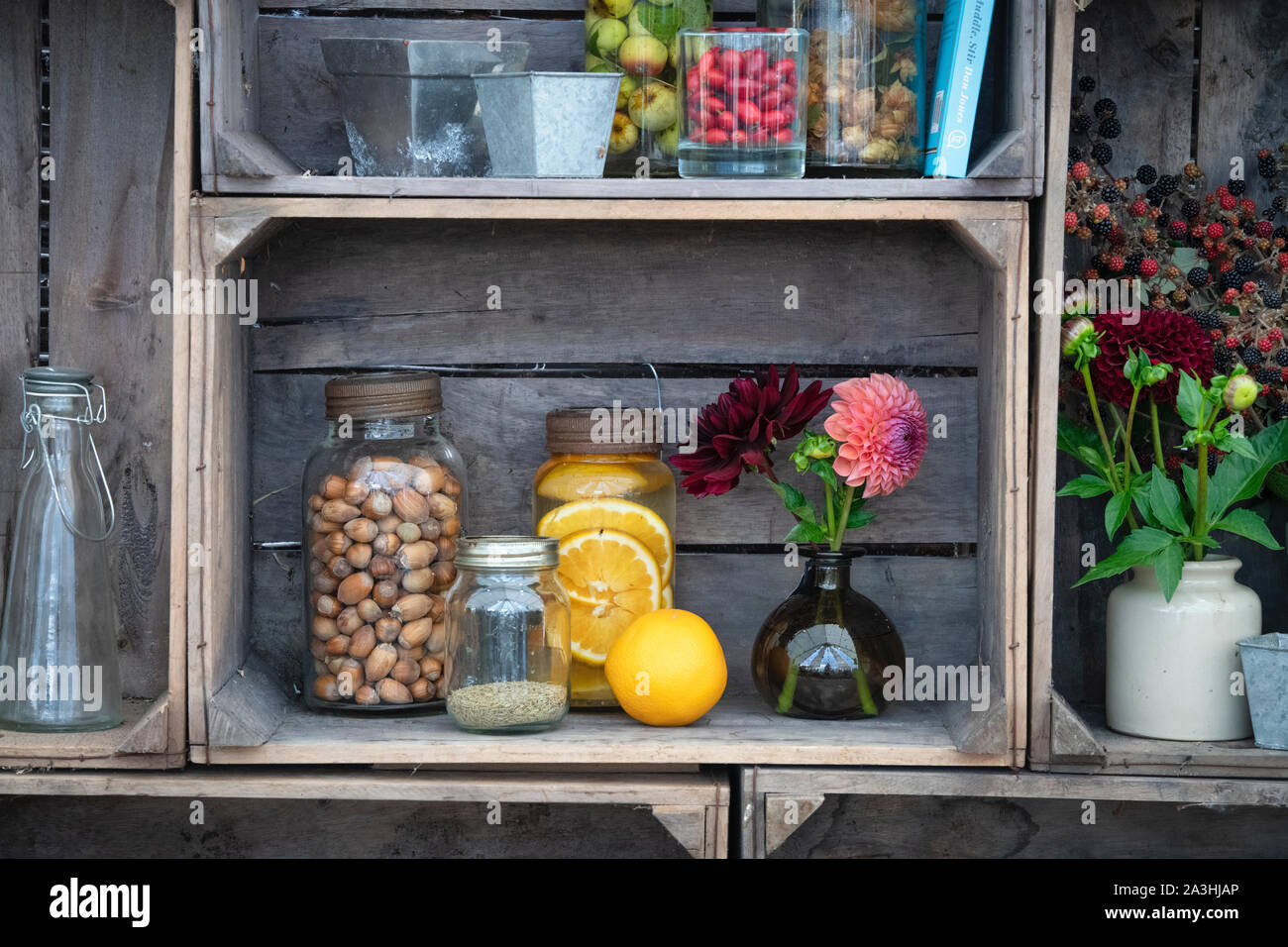 Old fashioned kilner gin jars infused with fruits and nuts with vases of cut flowers in a wooden crate display. UK Stock Photo