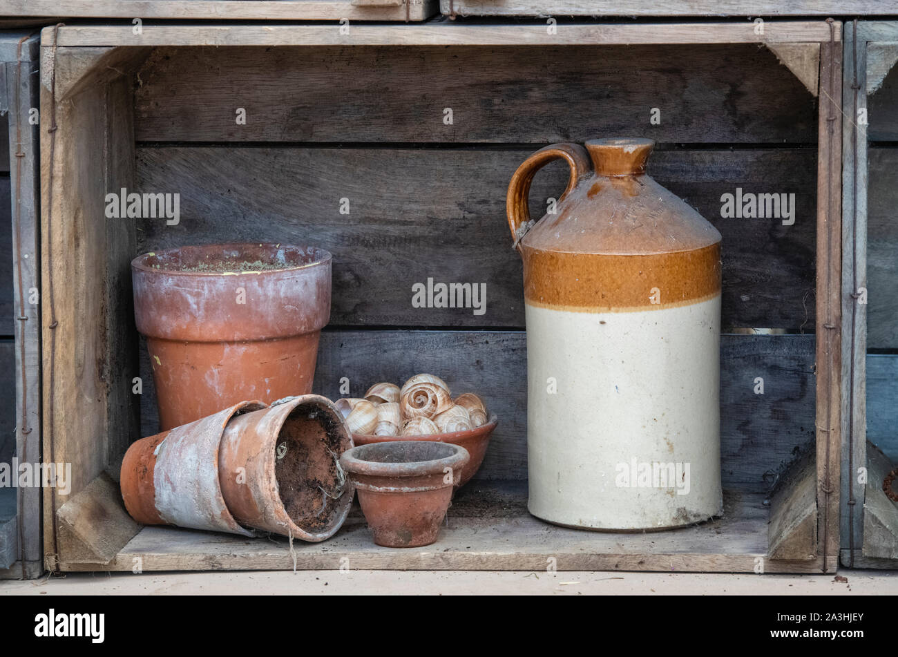 Stoneware jar and terracotta plant pots in a wooden crate shelf display. UK Stock Photo