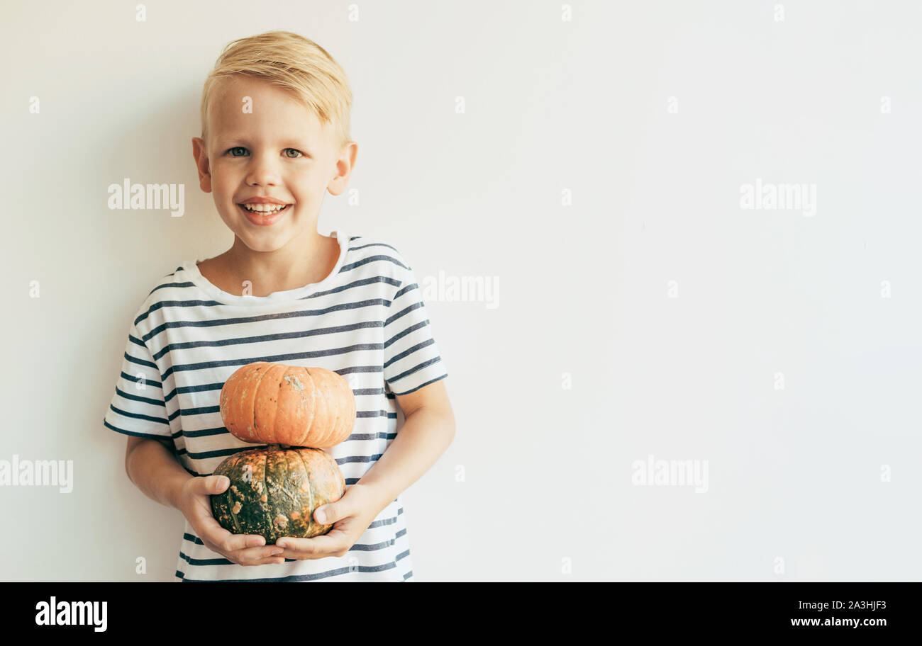 Blond cute Caucasian boy in a striped T-shirt with a ripe pumpkin Stock Photo