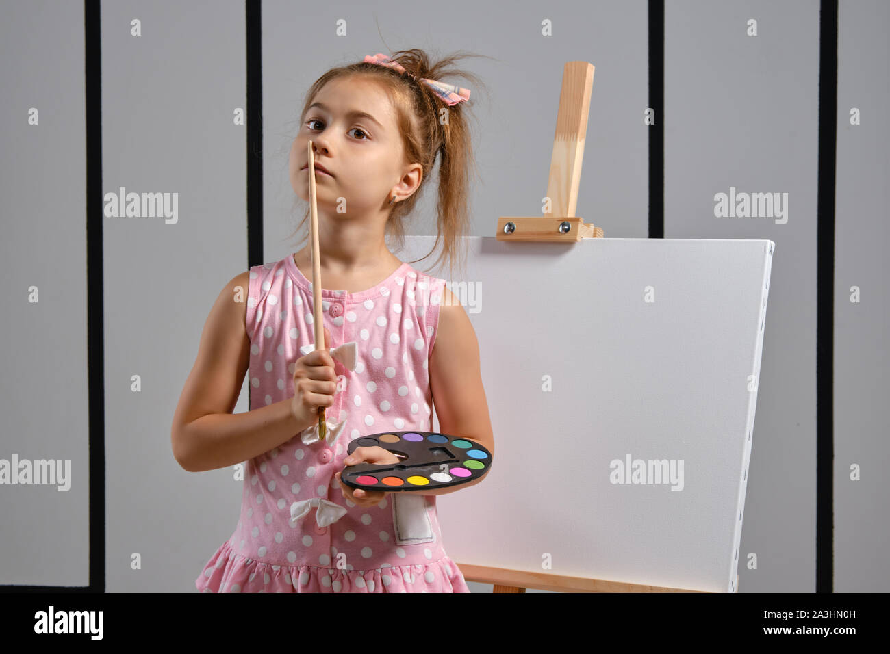 Little girl artist in a pink dress is standing behind easel and ...