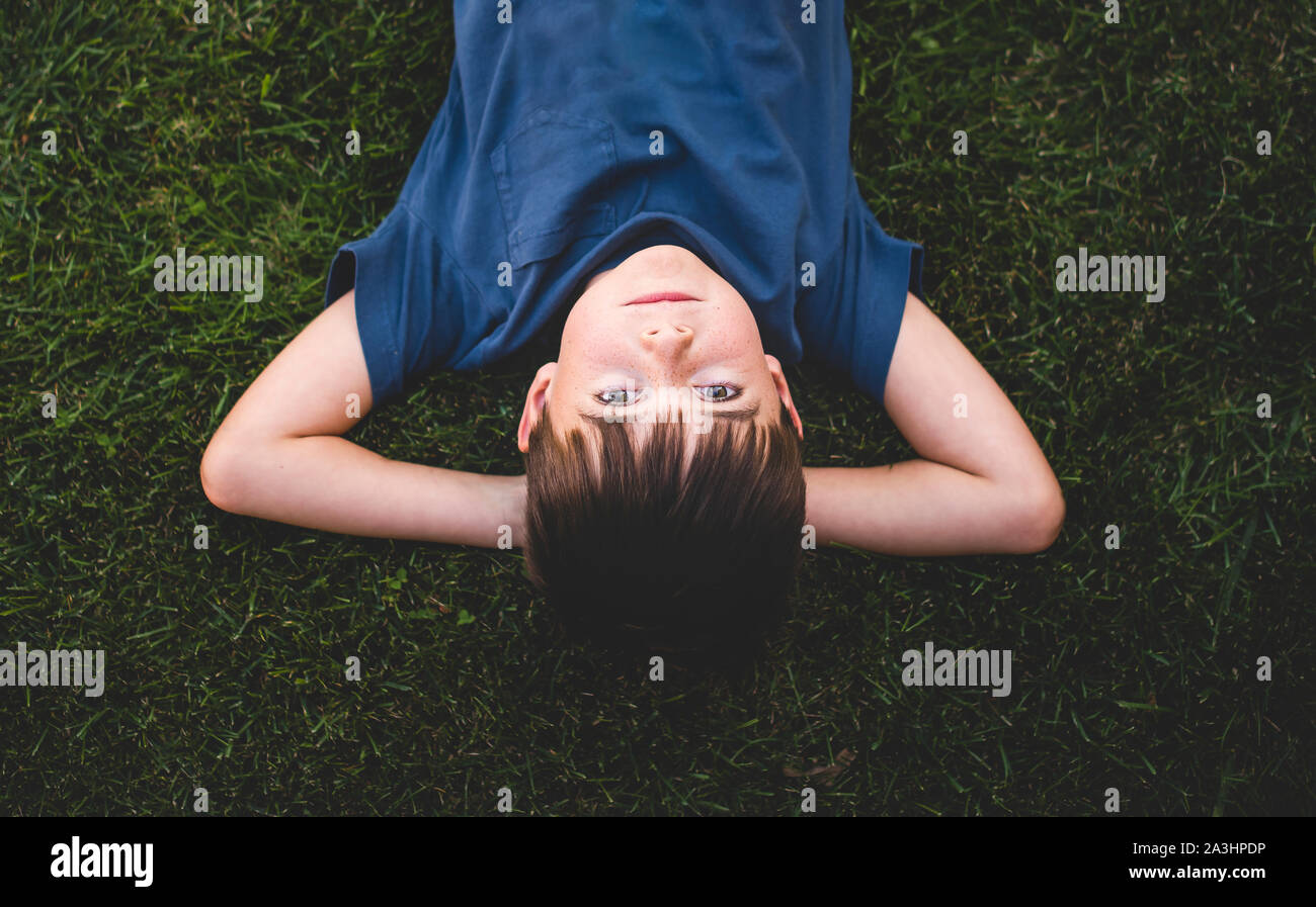 Upside down image of boy laying on grass with arms behind head. Stock Photo