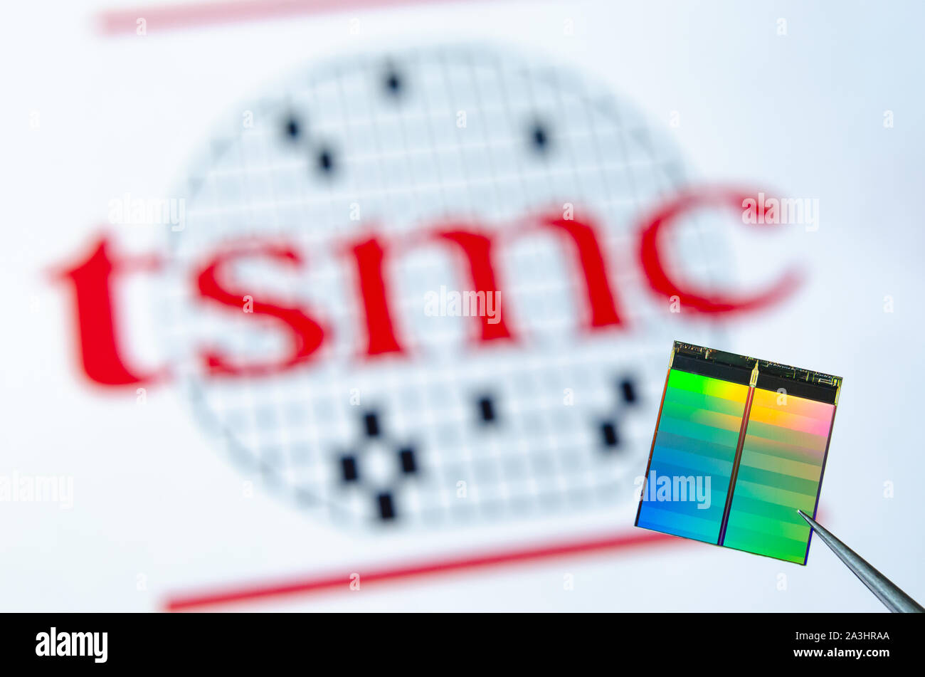 Close up photo of microchip (aka semiconductor chip, semiconductor device, Integrated Circuit) hold in tweezers with TSMC logo on a background. Stock Photo