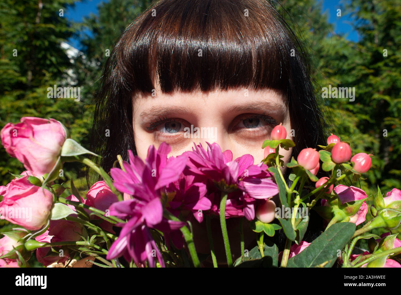 Portrait of Young Adult Woman Peering over Bouquet of Flowers Stock Photo