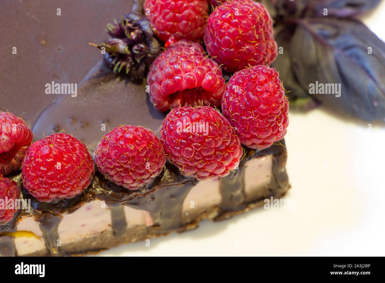 Diet sweets. Close up chocolate vegan cake with raspberries on white plate with basil leaves. Homemade natural product from harmless ingredients. Stock Photo