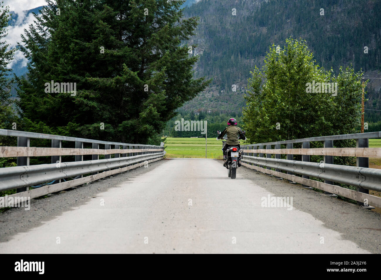 A woman rides her motorcycle across a bridge on a cloudy summer day. Stock Photo