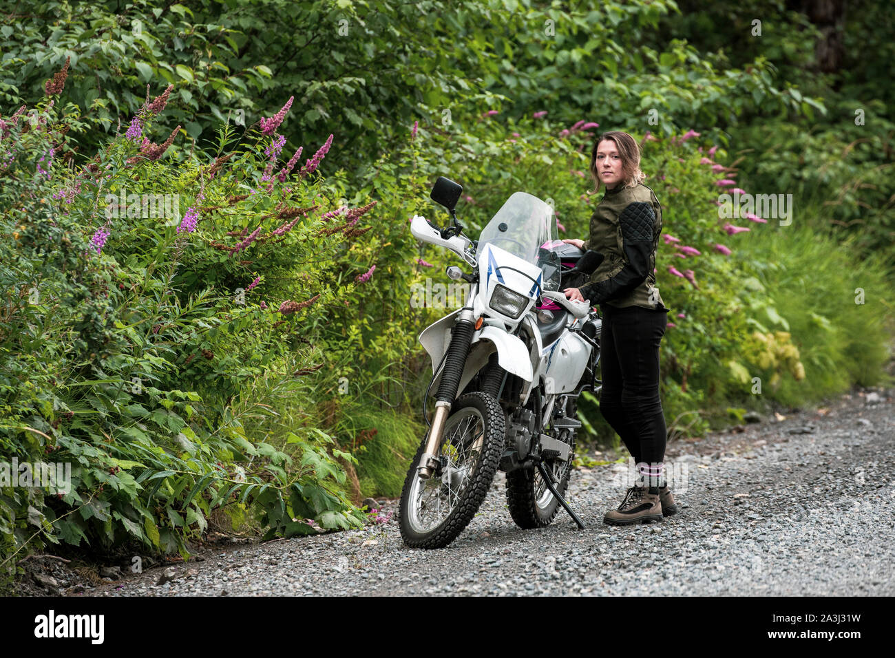 A women takes a break from motorcycle riding and stands with her bike. Stock Photo