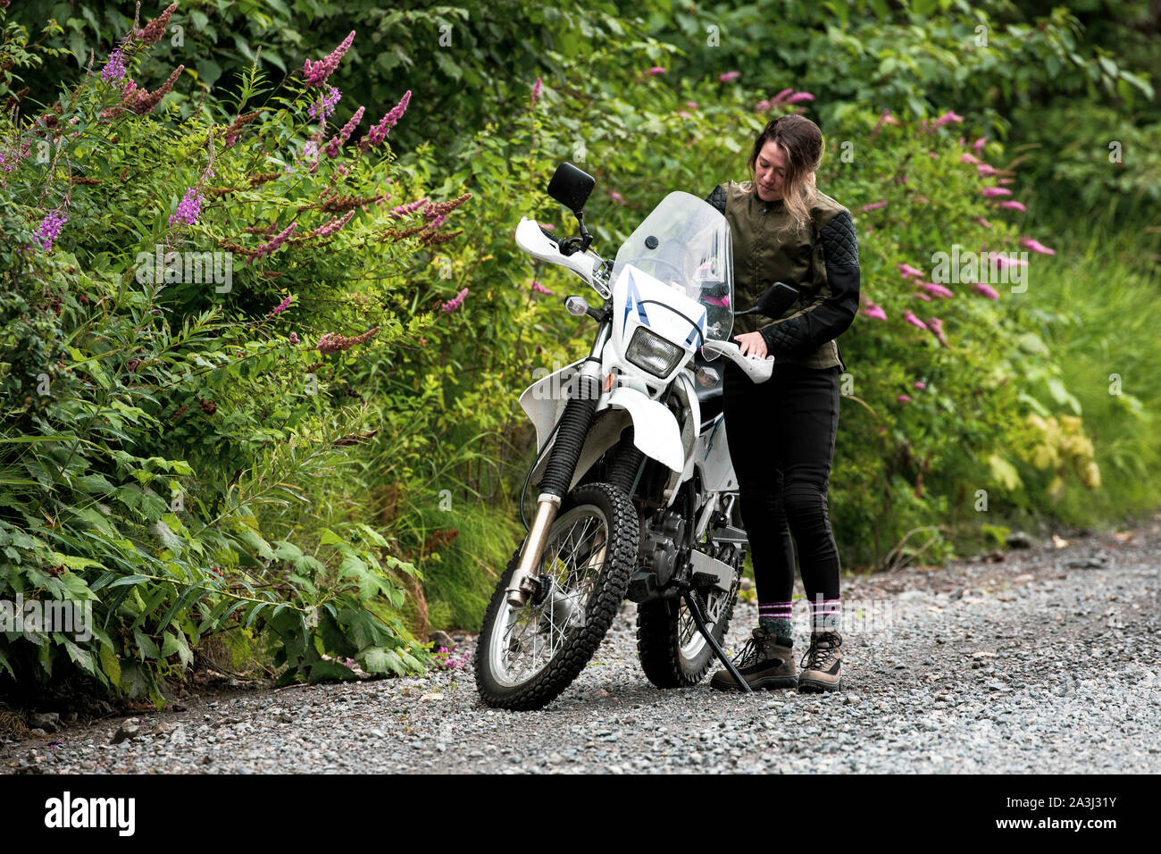 A women takes a break from motorcycle riding and stands with her bike. Stock Photo
