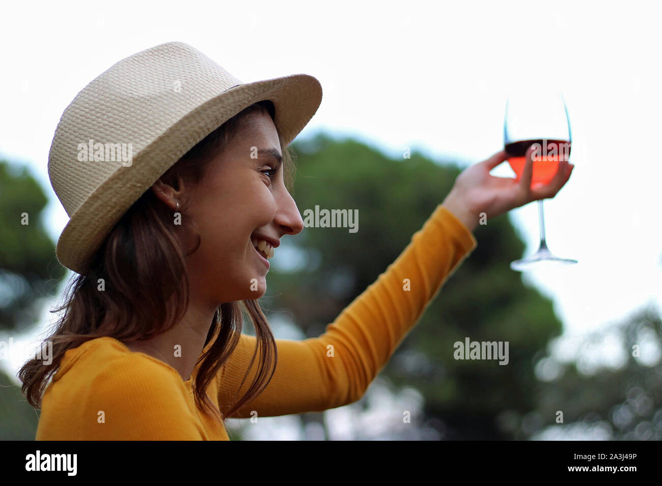 Young girl dressed in yellow and in a hat with a glass of rose wine ...