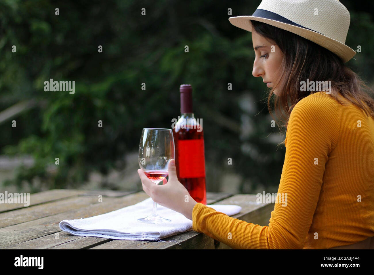 Young girl dressed in yellow and in a hat with a glass of rose wine ...