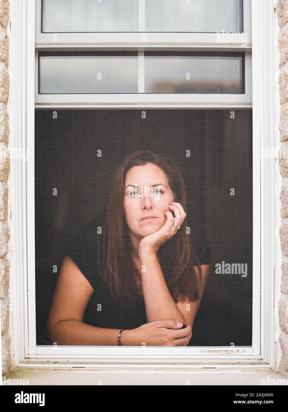 Woman looking out of open window with chin resting on hand. Stock Photo