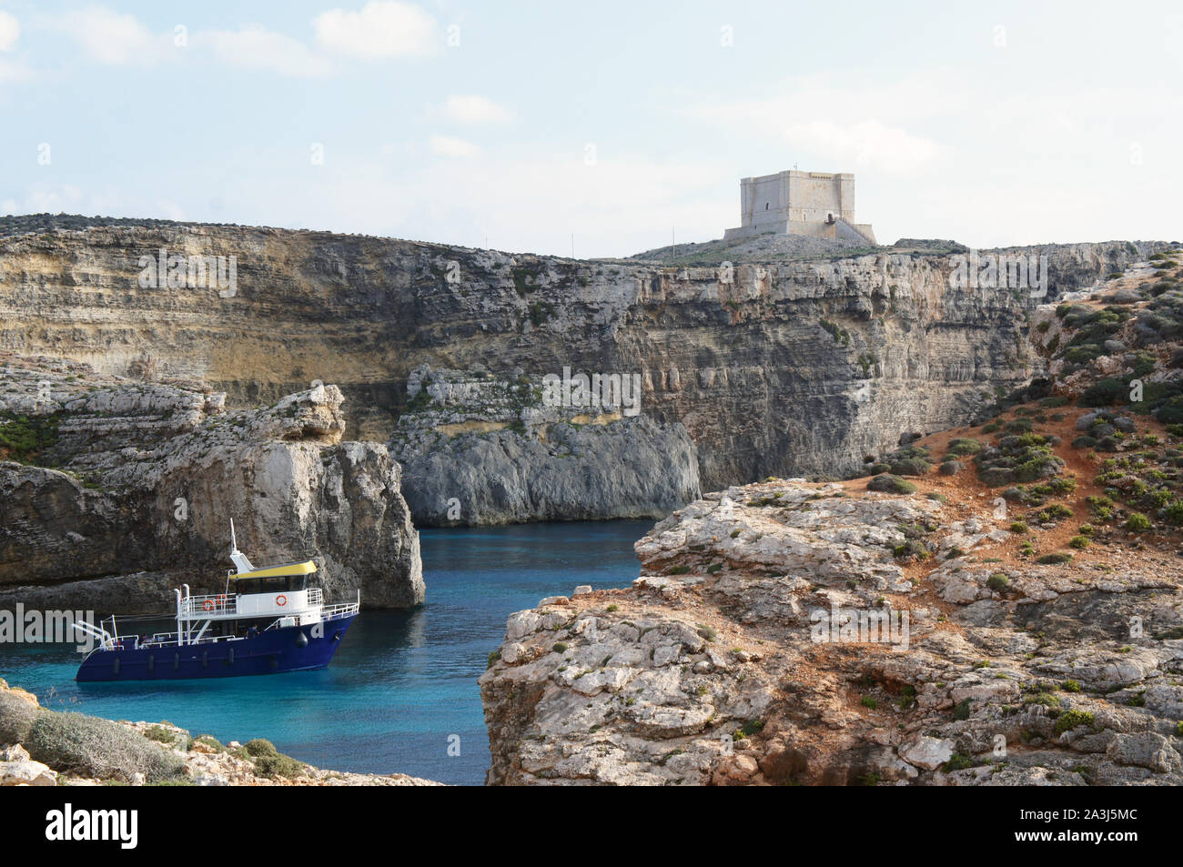 Single boat on the blue lagoon surrounded by rocky cliffs with a tower in the distant Stock Photo