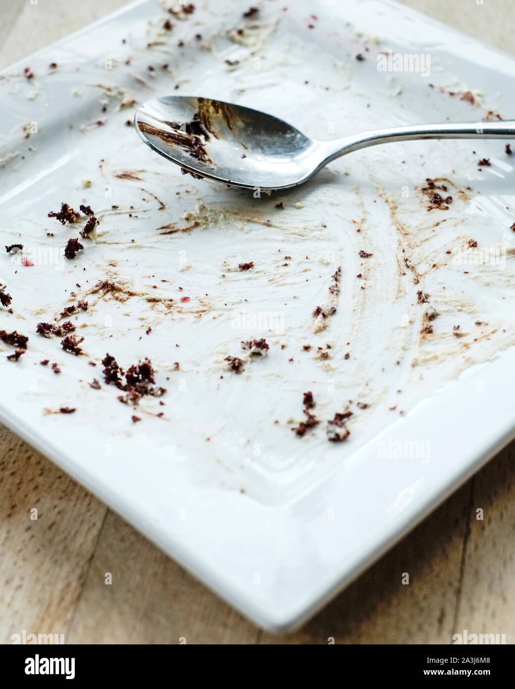 A spoon resting on an empty square plate after a chocolate dessert has been eaten in a restaurant. Stock Photo