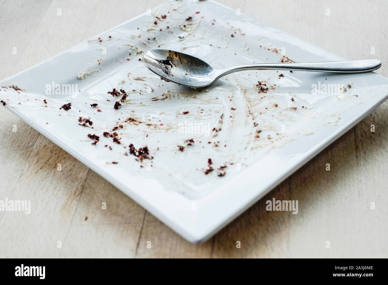 A spoon resting on an empty square plate after a chocolate dessert has been eaten in a restaurant. Stock Photo