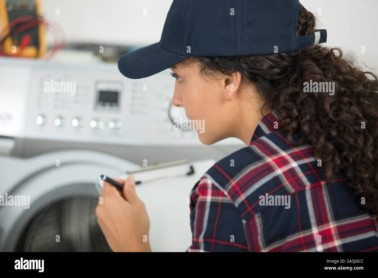servicewoman with clipboard looking at washing machine Stock Photo