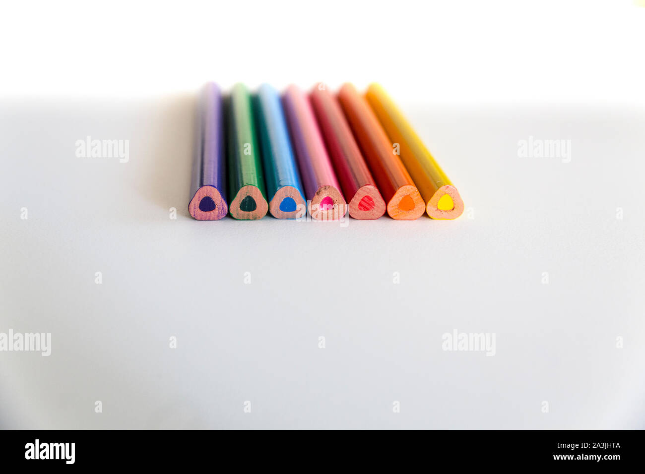 Close up of a number of colorful thick triangular prism crayons seen from their rear tips, arranged together on neutral white background with copy spa Stock Photo