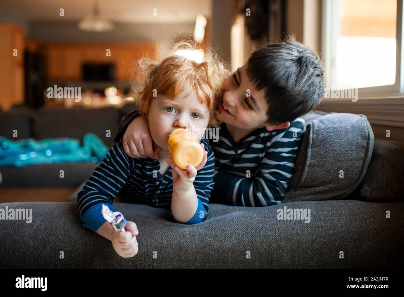 Brothers sitting on couch together with arms around each other at home Stock Photo