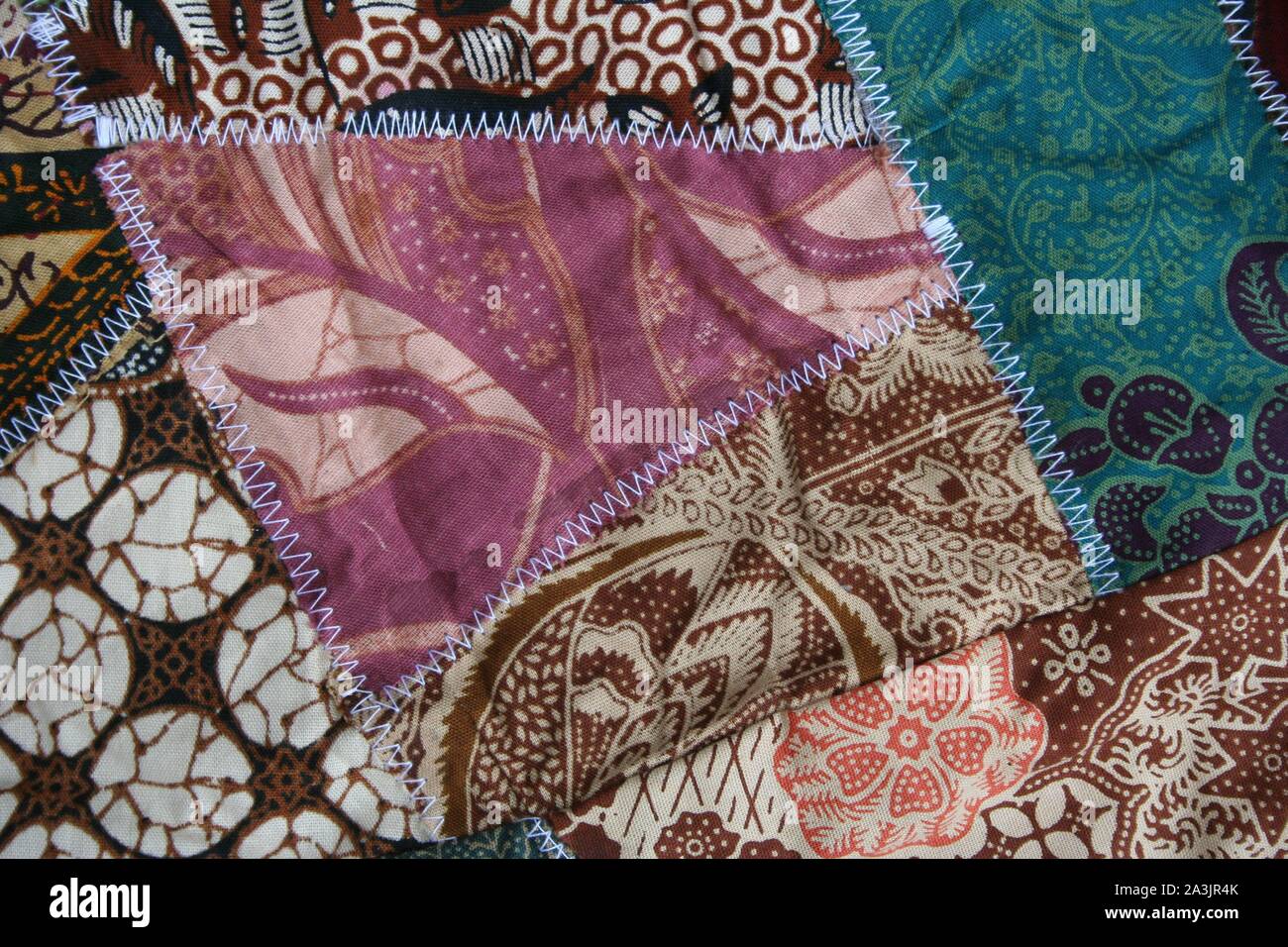 Batik material background, Indonesian material pieced together with white zigzag stiches in crazy quilt design in colorful blue green pink and brown c Stock Photo