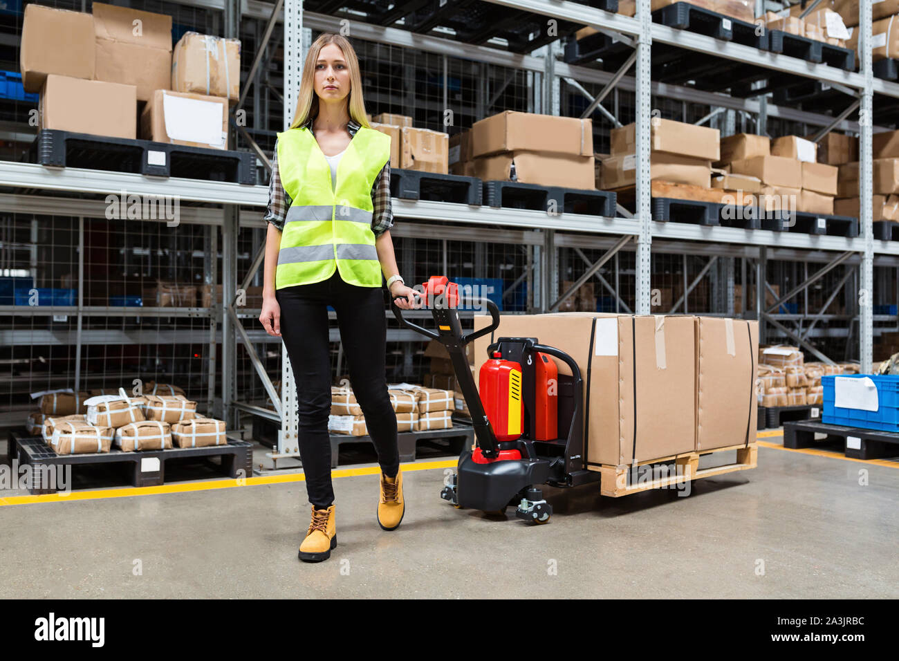 Warehouse worker dragging hand pallet truck or manual forklift with the