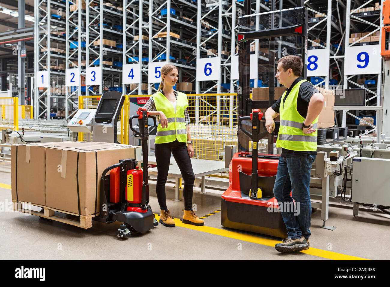 Storehouse employees in uniform standing near pallet truck and forklift