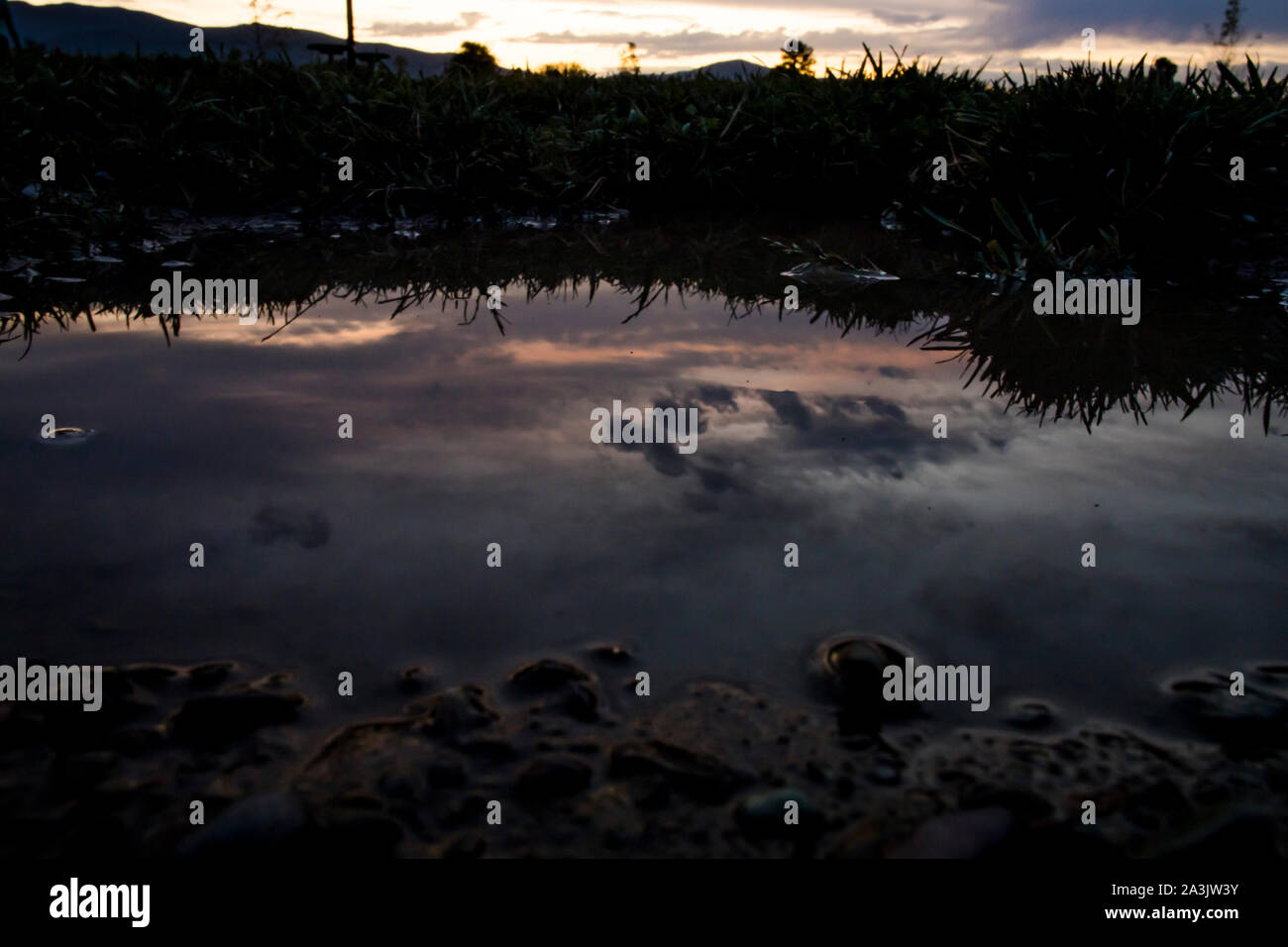A reflection of clouds in a puddle at sunset Stock Photo