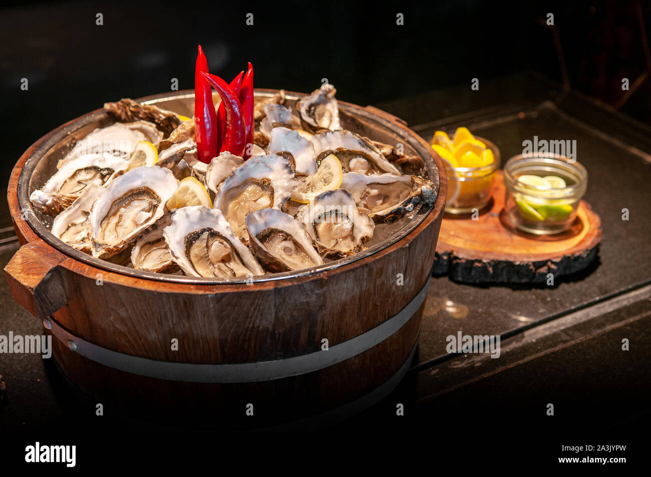 Fresh whole marine Fine de claire oysters in oak wood bucket with lime and lemon - dark tone food image Stock Photo