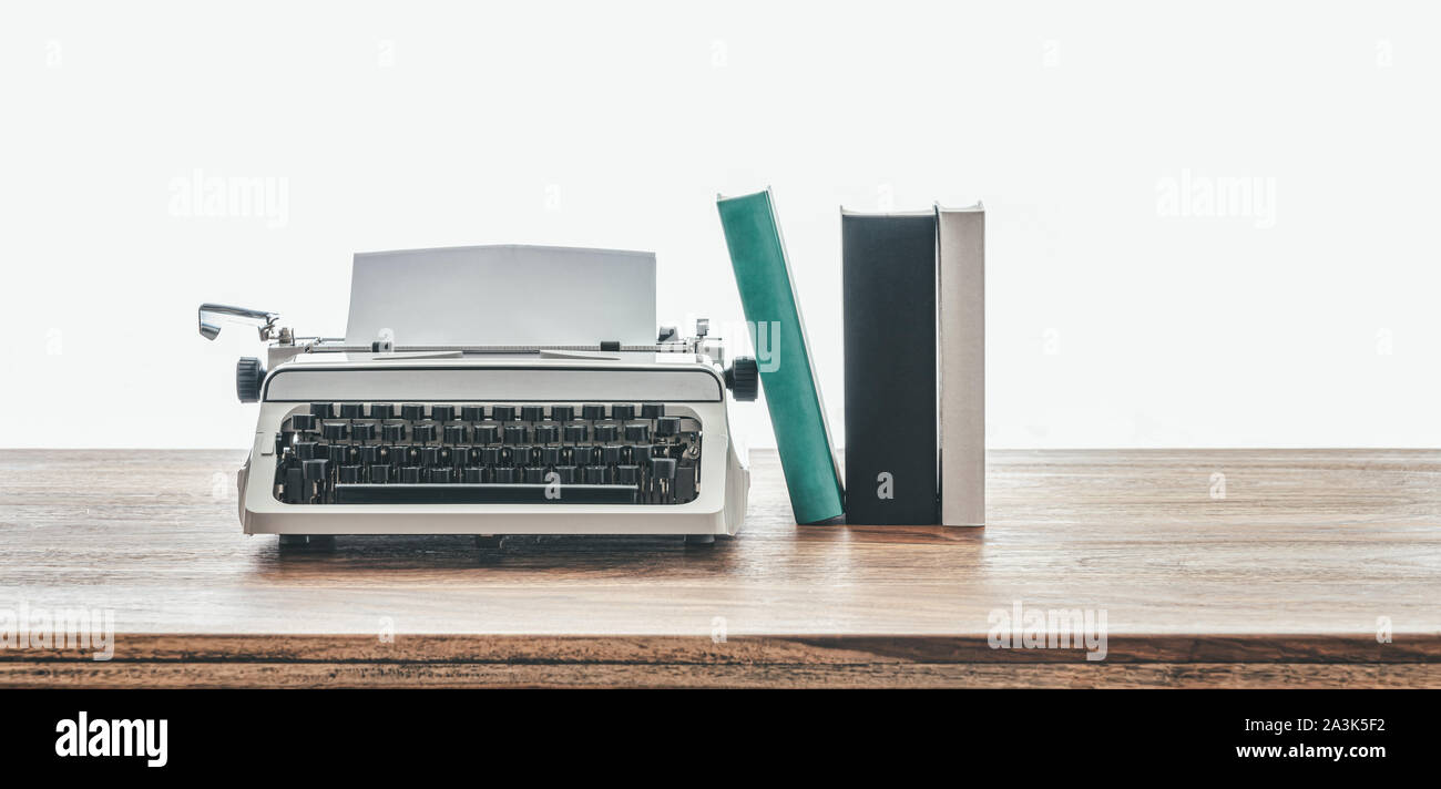 close-up low angle view of vintage typewriter and books on rustic wooden table against white background Stock Photo