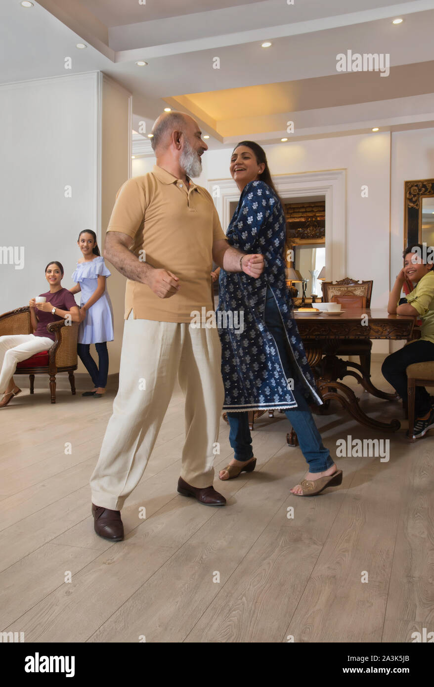 Grandparents dance in the living room in front of the family. Stock Photo