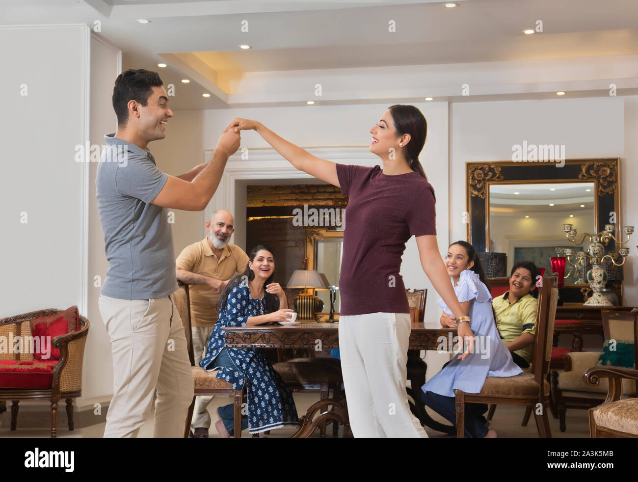 Young couple dances in the living room while the family watches. Stock Photo