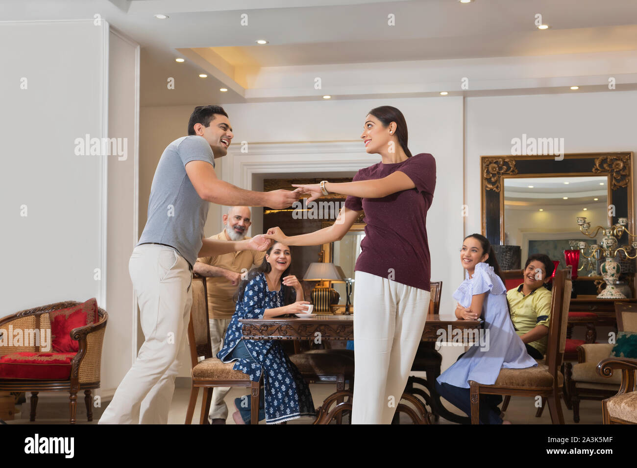 Young couple dance in the living room while the family watches. Stock Photo