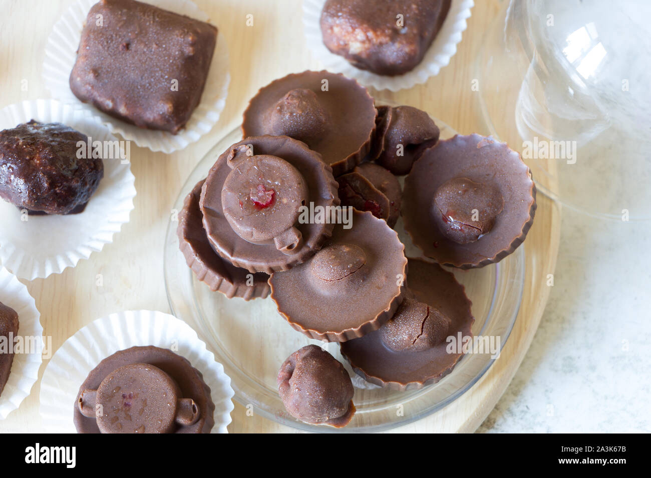 Homemade raw chocolate sweet candies with raspberries inside with droplets of water and raspberry juice on surface. Flat lay. Top view. White wraper. Stock Photo