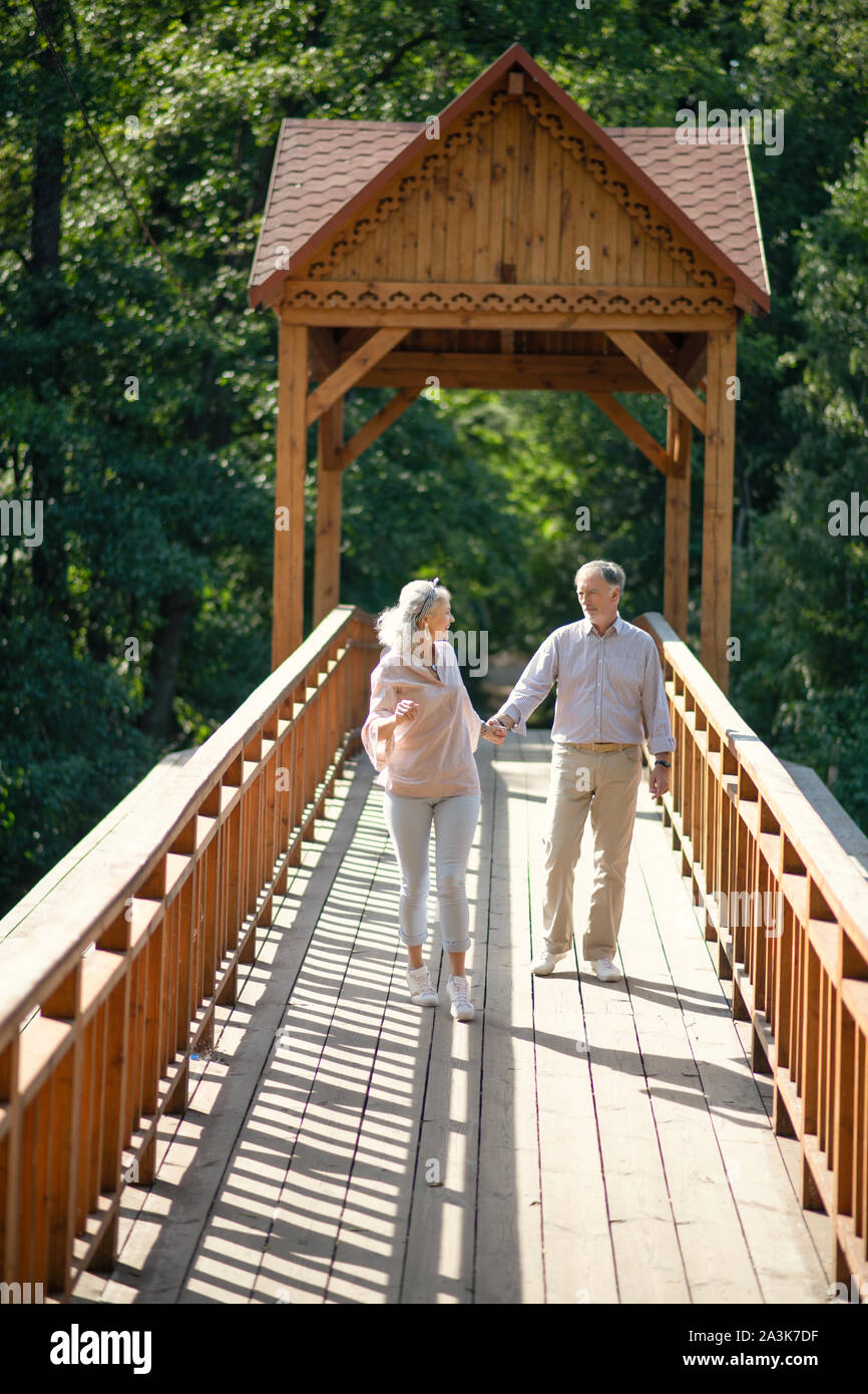 Mature adults walking hand in hand on nice bridge in the park Stock Photo