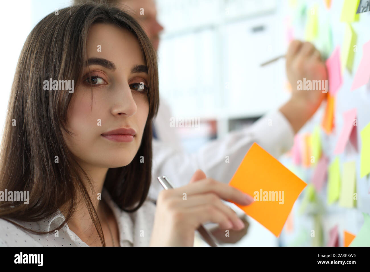 Pretty female office worker holding sticky paper looking in camera Stock Photo