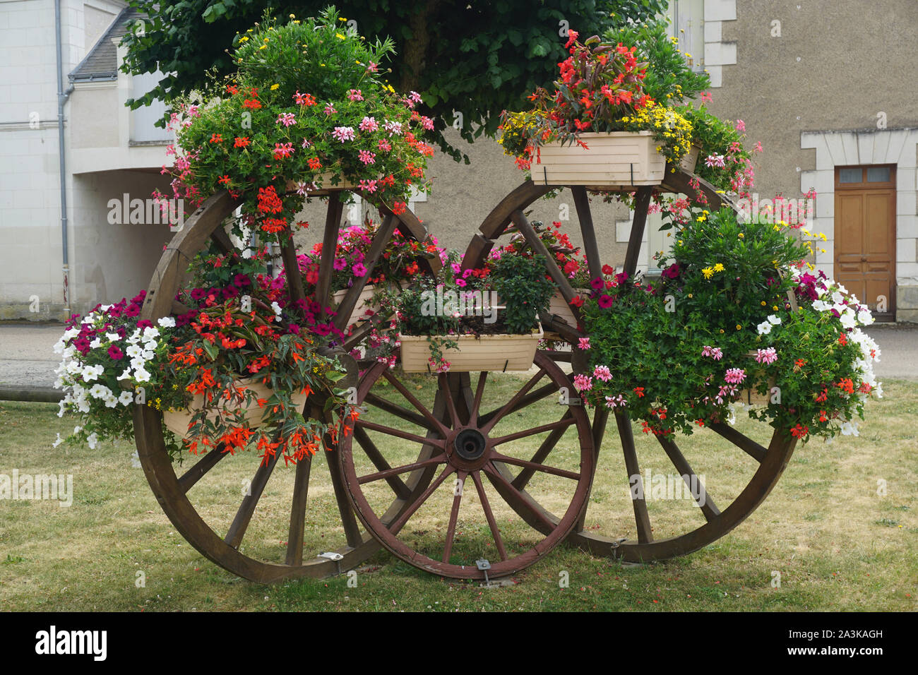 colorful flower pots hanging on wood carriage wheels as decoration in a small village in France Stock Photo