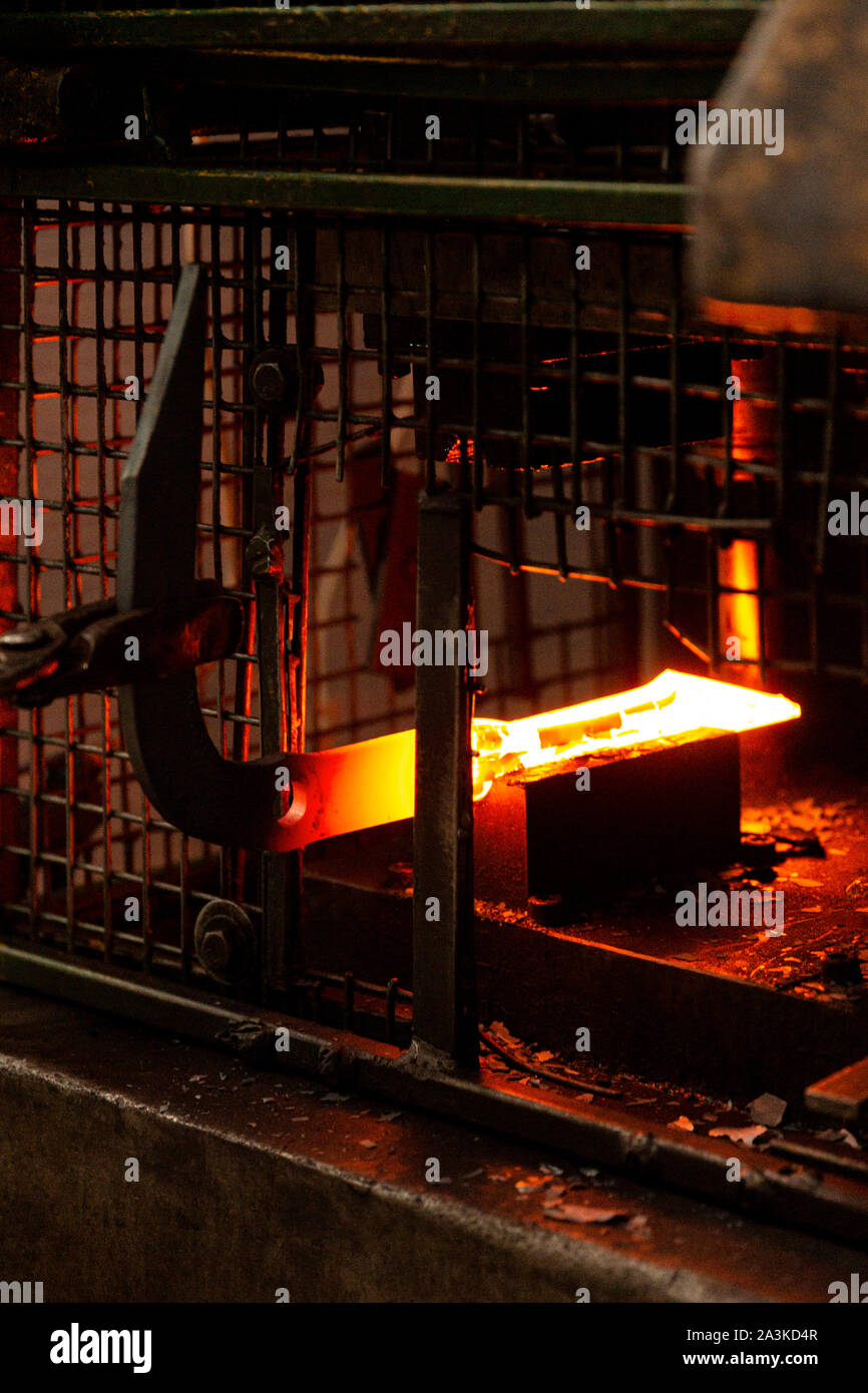 Fiery hot metal bar being tapped into shape by metal fabricator. Stock Photo