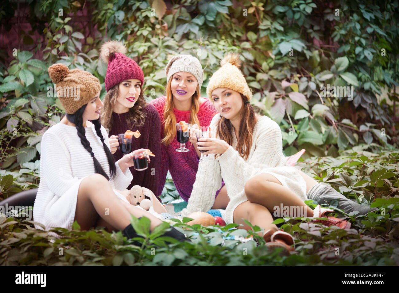 Young women drink mulled wine in autumn park. Sunny autumn day. Outdoors lifestyle fashion portrait. Positive emotions. Stock Photo