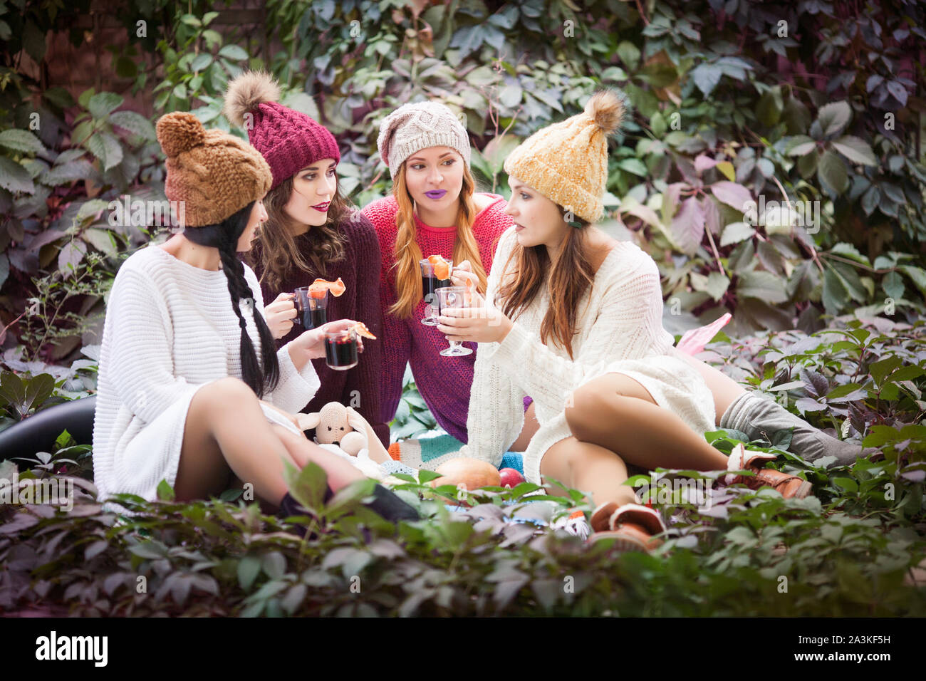 Young women drink mulled wine in autumn park. Sunny autumn day. Outdoors lifestyle fashion portrait. Positive emotions. Stock Photo