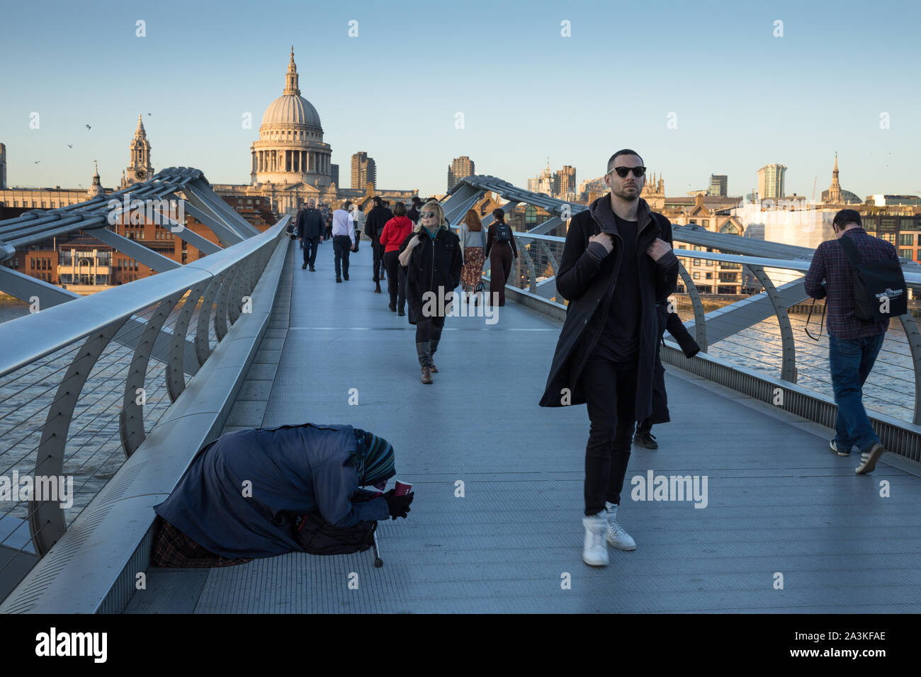 Pedestrians walking past a beggar on the Millenium Bridge with St Paul's Cathedral beyond, London, England, UK Stock Photo