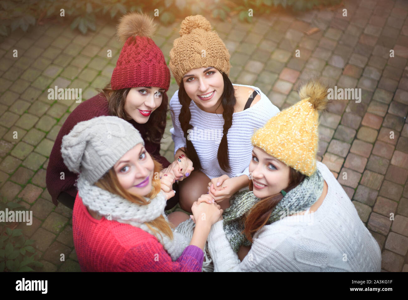 Girls in warm knitted clothes and hats hug, top view. Autumn day, a group of friends. Positive emotions. Stock Photo
