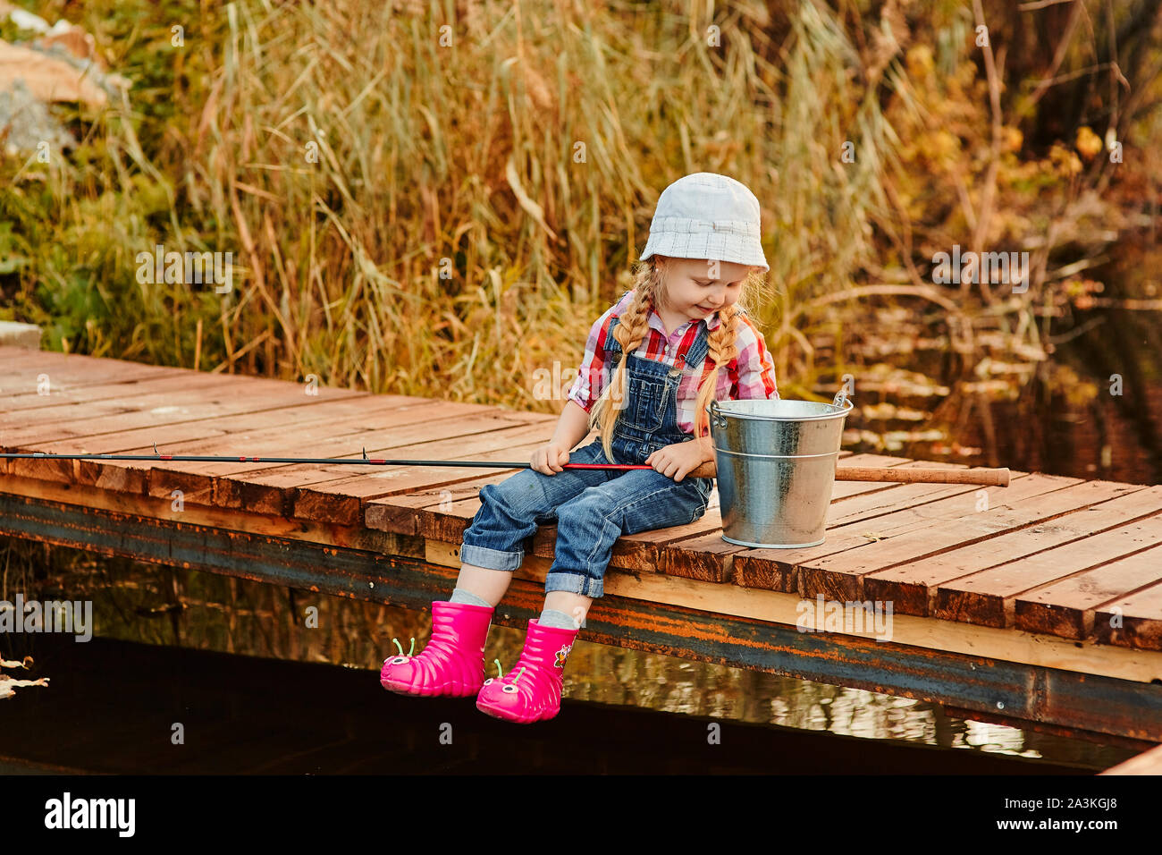 A little girl with a fishing rod looks at the catch of fish in a bucket  Stock Photo - Alamy