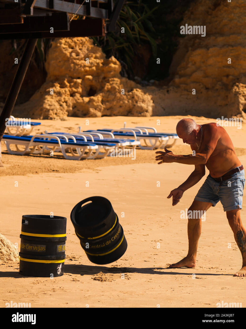 A working man deliver barrels of beer by hand to a beach restaurant on a hot summer day in Olhos D'Agua, Algarve, Portugal Stock Photo