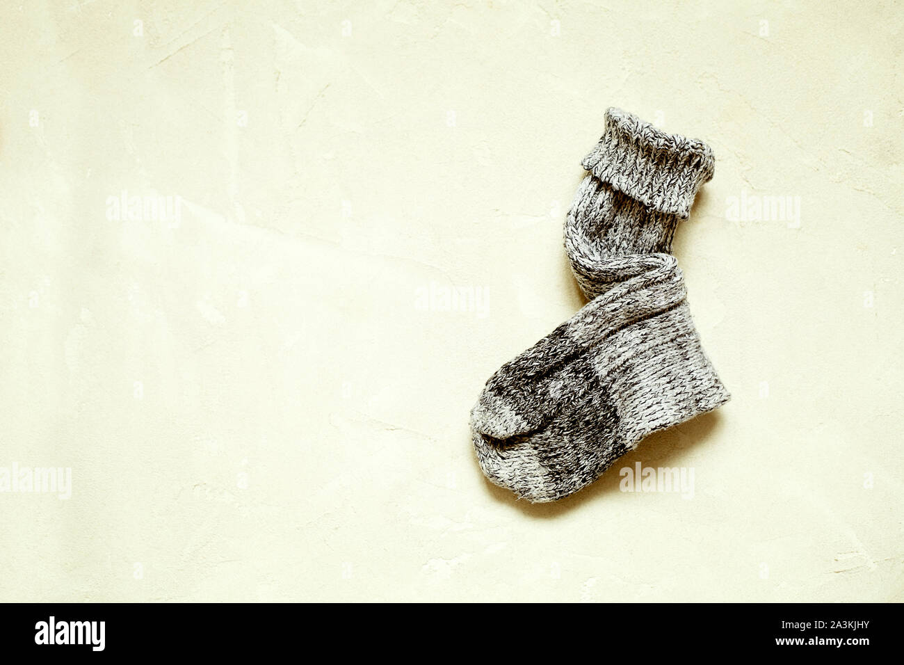 Handmade warm knitted sock grey color on textured background with copy space.Winter and autumn concept of eco clothes.Minimalism Kinfolk Style Stock Photo