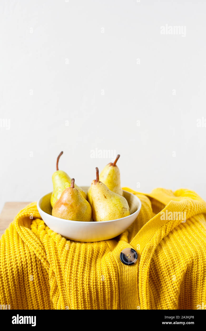 Organic yellow pears in white bowl on yellow knitting sweaters and white wall background with copy space.Rural minimalistic still life.Kinfolk style Stock Photo